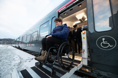 Kvinne i rullestol går av toget på en rampe