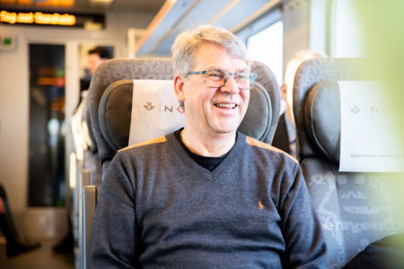 Eldre mann sitter på toget og smiler