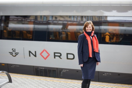 Kvinnelig konduktør står foran toget og smiler
